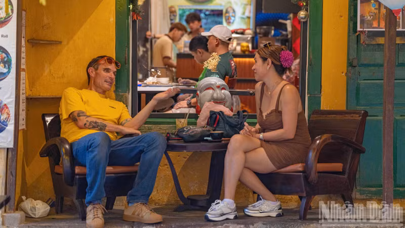 Two visitors sit and converse leisurely, observing the rhythm of life in Hoi An through time-worn windows.