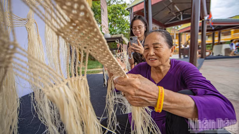 Visitors observe an artisan meticulously weaving a hammock from fibres of the Chinese parasol tree.