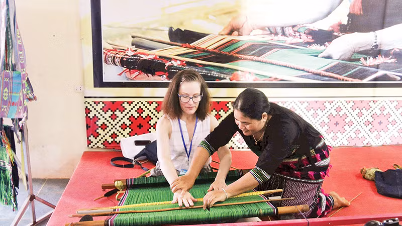 Artisan H’Binh introduces Ma brocade weaving techniques to foreign visitors at the cooperative. (Photo: nhandan.vn)