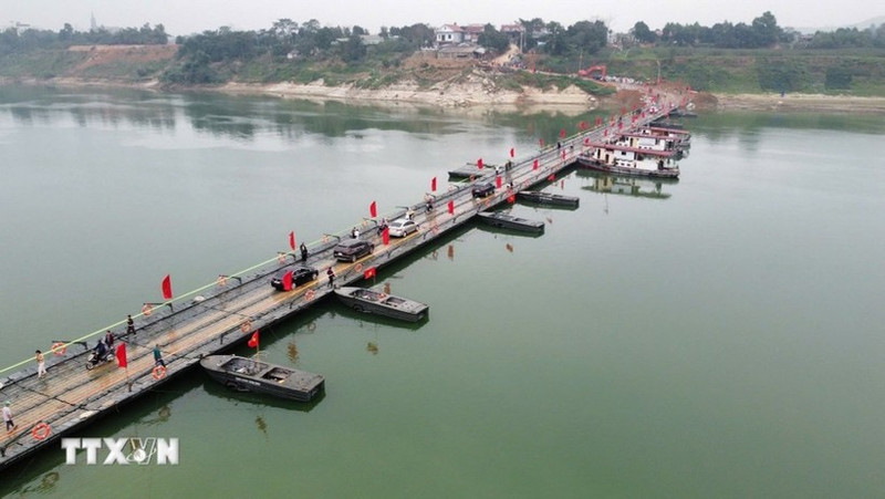 People and vehicles travel across the Lo river pontoon bridge on the morning of February 16. (Photo: VNA)