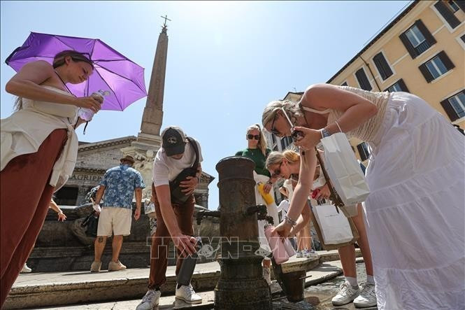 People collect drinking water to cool down on a hot day in Rome, Italy. (Photo: Xinhua/VNA)