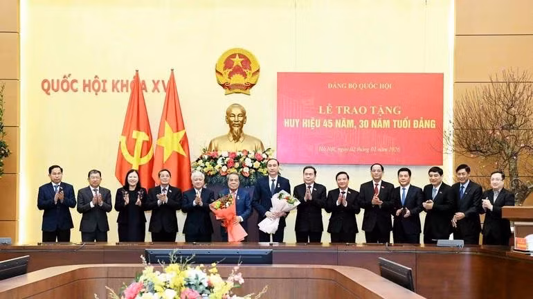 National Assembly Chairman Tran Thanh Man and officials congratulate Duong Thanh Binh and Phung Khanh Tai (with flowers) on being awarded 45-year and 30-year Party membership badges. (Photo: nhandan.vn)