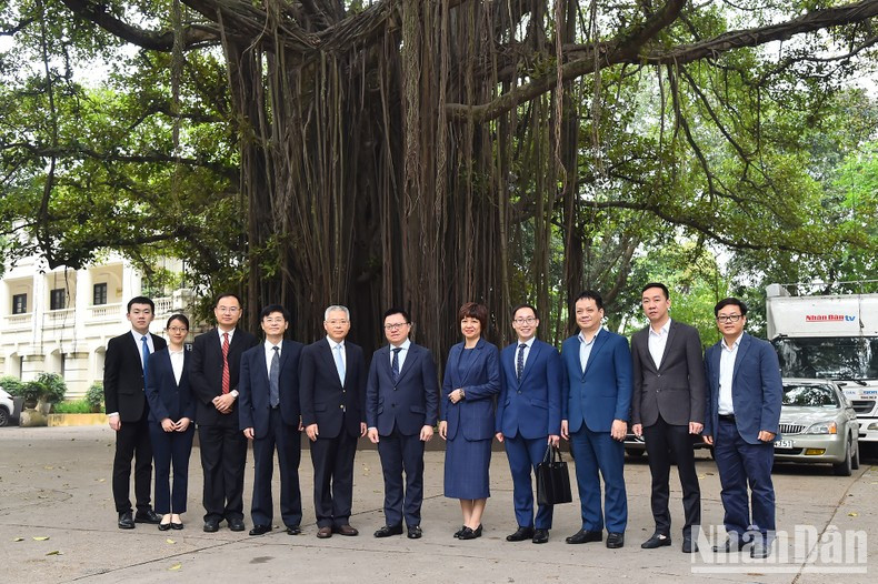Le Quoc Minh, Hu Zhaoming and other delegates take photos beside the banyan tree at Nhan Dan Headsquarters.