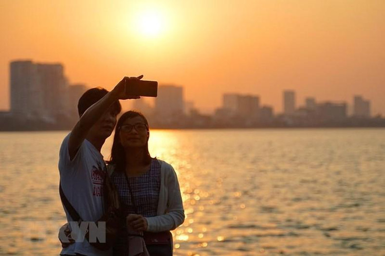 Young people save the autumn moment in Hanoi at West Lake. (Photo: Khanh Hoa/VNA)
