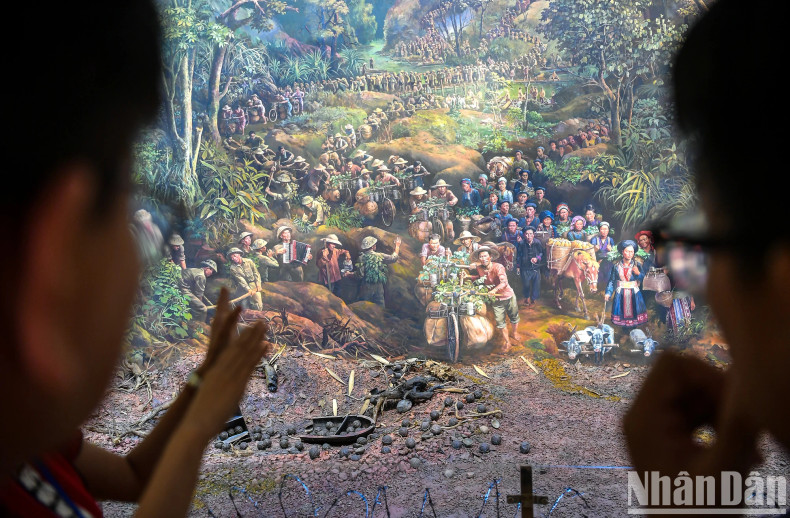 The tour guide leads viewers to each segment of the painting. In the photo is the first scene "All the people go to war" with images of overlapping groups of people, soldiers carrying goods, climbing mountains and wading streams to provide food for the front line. The tour guide leads viewers to each segment of the painting. In the photo is the first scene "All the people go to war" with images of overlapping groups of people, soldiers carrying goods, climbing mountains and wading streams to provide food for the front line.