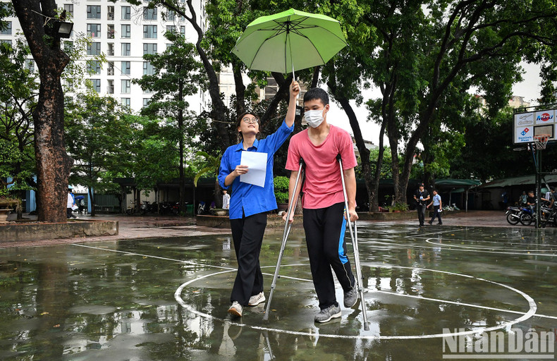 A youth volunteer holds an umbrella over Ha Duy Toan, who had to come to the exam venue on crutches because he unfortunately broke his leg right before the exam. A youth volunteer holds an umbrella over Ha Duy Toan, who had to come to the exam venue on crutches because he unfortunately broke his leg right before the exam.