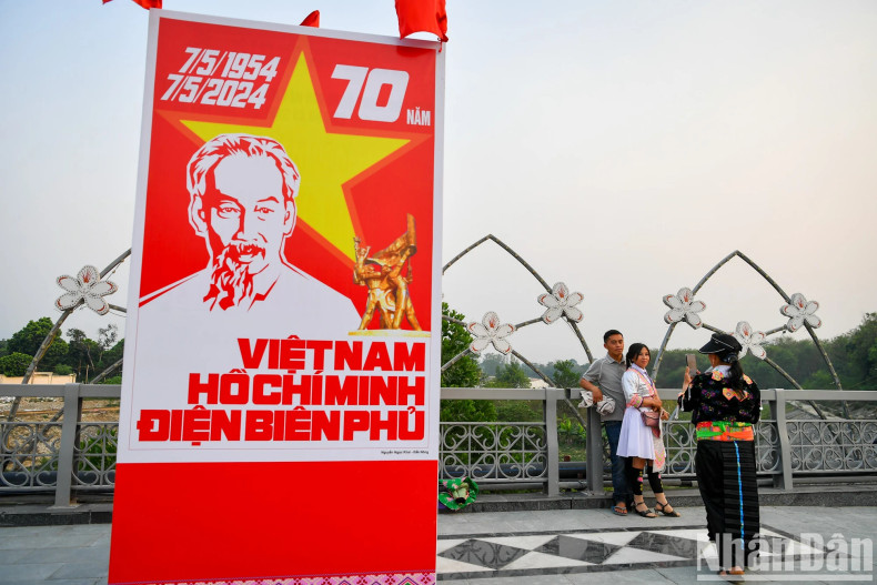 People take photo next to a giant poster featuring portrait of President Ho Chi Minh, and words saying “Vietnam – Ho Chi Minh - Dien Bien Phu”.