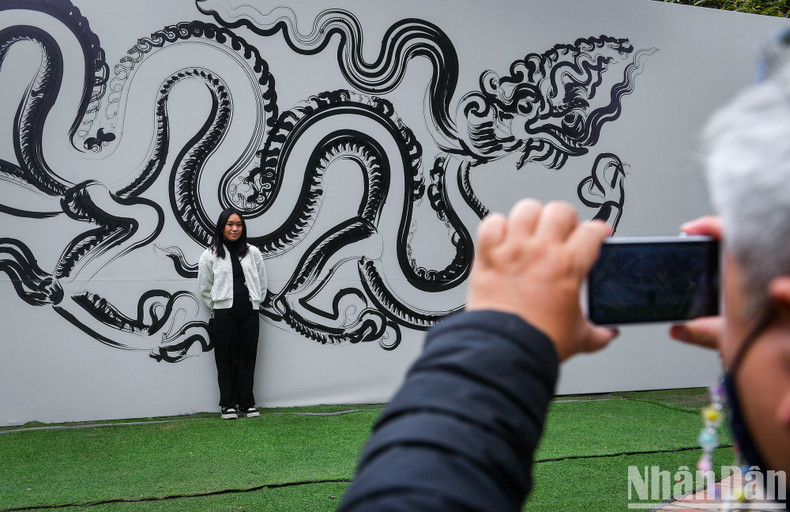 A girl poses in front of a giant calligraphy work featuring the dragon.