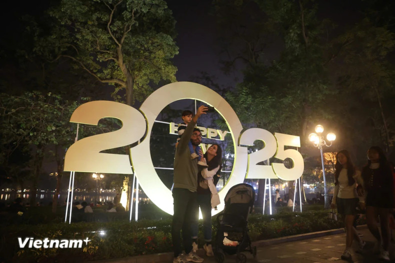 Foreign tourists take a selfie photo in front of a decorative design celebrating the New Year 2025 near Hoan Kiem Lake. (Photo: VN+) Foreign tourists take a selfie photo in front of a decorative design celebrating the New Year 2025 near Hoan Kiem Lake. (Photo: VN+)