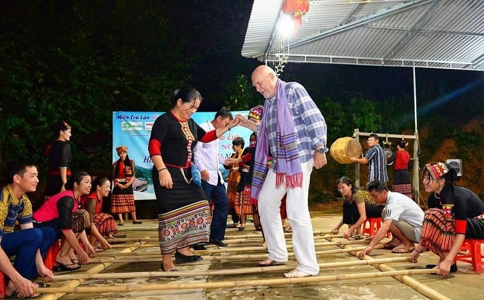 A foreign visitor joins a bamboo pole dance with a local ethnic woman in Khe Ran Village