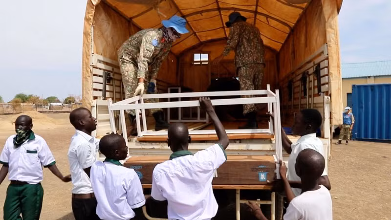 Members of Construction Team 2 and students unload the donated desk-bench sets at Abyei Primary School.