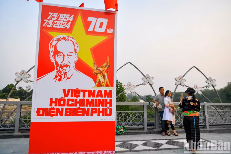 People take photo next to a giant poster featuring portrait of President Ho Chi Minh, and words saying “Vietnam – Ho Chi Minh - Dien Bien Phu”.