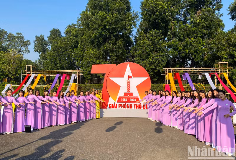 Women in ao dai pose for a photo in front of a large billboard celebrating the 70th anniversary of Hanoi’s liberation.