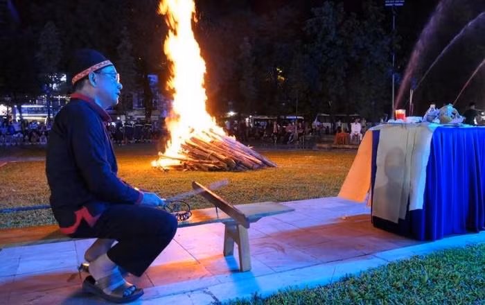 As the fire breaks out, artisan Sin Van Duong of Tan Bac Commune, Quang Binh District, arranges offerings, offers incense, and reads prayers, holding a bamboo stick in his left hand and a silver ring in his right hand to knock on the Pan do (a form of traditional musical instrument).