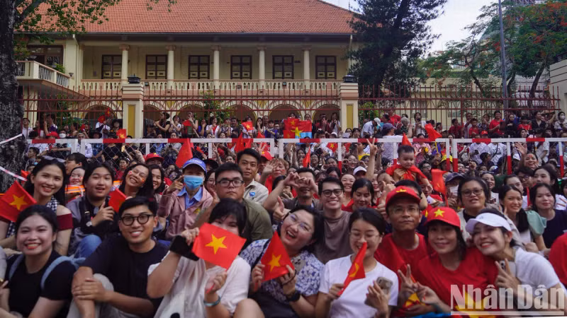 Children, accompanied by their parents, wave national flags and give smiles as they waite for the parade to approach.