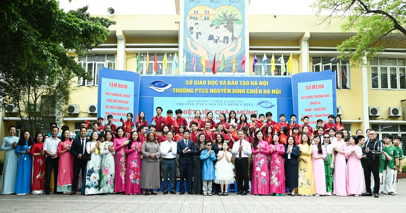 The two spouses pose for a commemorative photo in the schoolyard with teachers and students of Nguyen Dinh Chieu School.