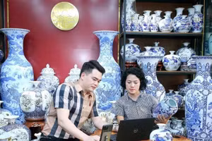 Artisan Tran Trung Hieu (Bat Trang Commune, Gia Lam District, Ha Noi) shares with a fellow artisan the process of listing products on e-commerce platforms. (Photo: HUY HOANG)