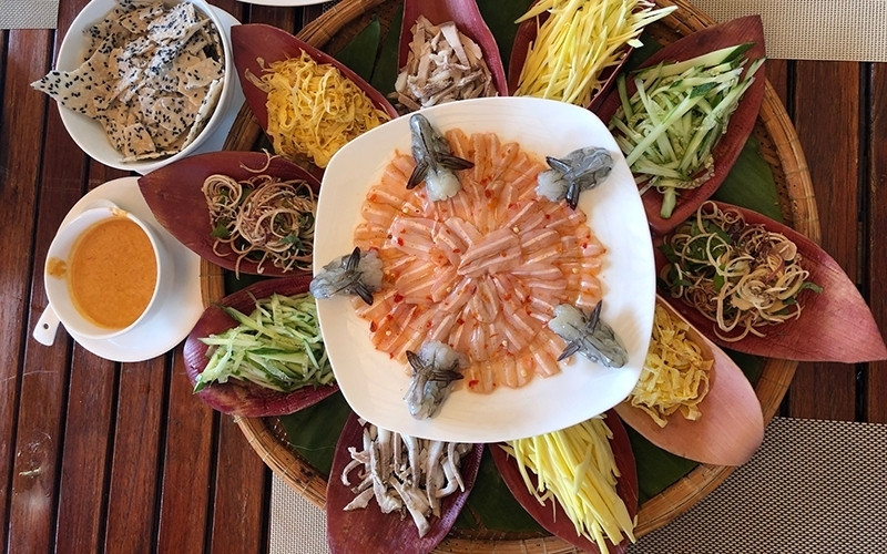 The dish is presented in a round bamboo tray filled with banana leaves, with a plate of spadefish fillets placed at its centre