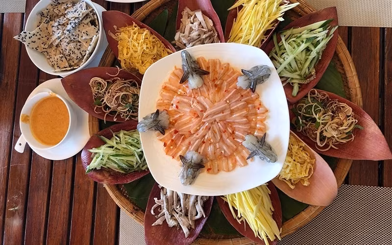 The dish is presented in a round bamboo tray filled with banana leaves, with a plate of spadefish fillets placed at its centre