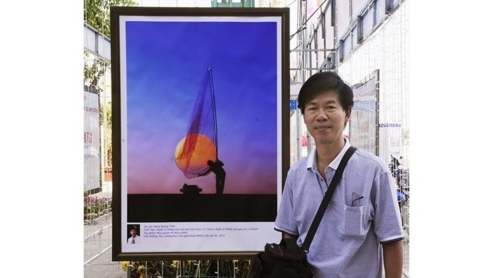 Photographer Dang Quang Vinh with one of his works. (Photo: NDO)