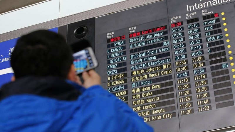 A man takes a picture of a flight information board displaying the scheduled time of arrival of Malaysia Airlines flight MH370 (top, in red) at the Beijing Capital International Airport in Beijing on March 8, 2014. (Credit: AFP)