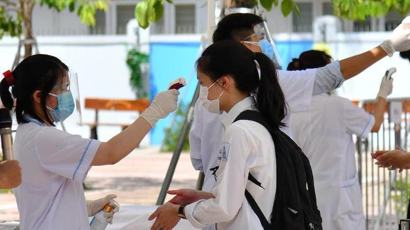 A student has her body temperature checked before entering the exam room.