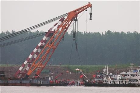 Medical workers, in white, stand as rescuers work on the capsized ship, center, on the Yangtze River in central China's Hubei province Thursday, June 4, 2015. Rescuers cut into the upside-down hull of the river cruise ship and pulled out drowned passengers early Thursday. (AP Photo/Andy Wong)