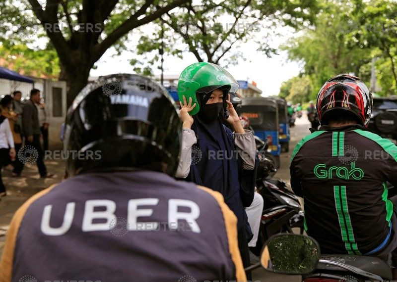 A passenger of Grab bike fixes her helmet next to Uber driver at Manggarai train station in Jakarta, Indonesia, March 26, 2018. (Photo:Reuters)