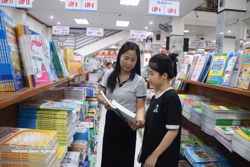 A parent chooses textbooks for her daughter ahead of the new school year. (Photo: VNA)