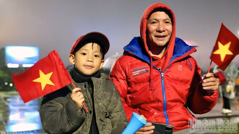 Two generations of a family brave the rain and cold together to celebrate the team's victory. (Photo: Mai Van Bao)