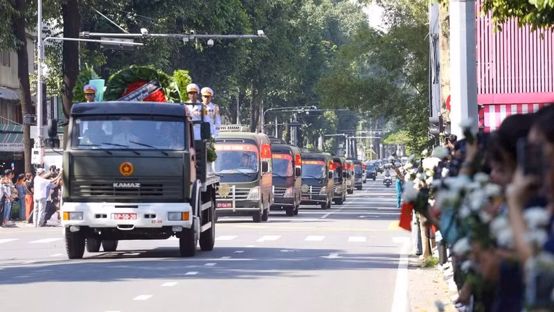 The convoy carrying the remains of fallen soldiers passes lines of people holding white chrysanthemums along the roadside. (Photo: THE ANH)