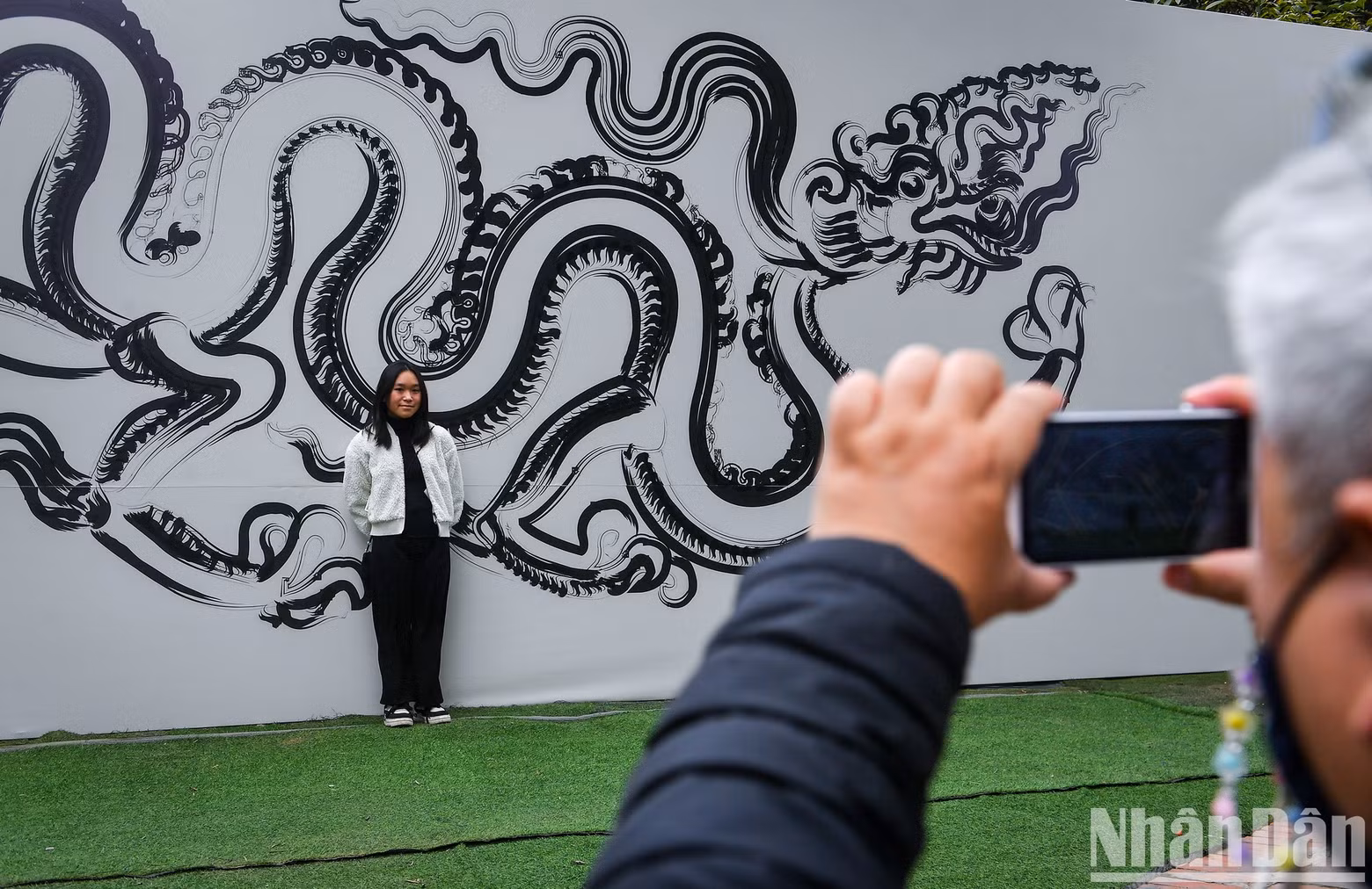 A girl poses in front of a giant calligraphy work featuring the dragon.
