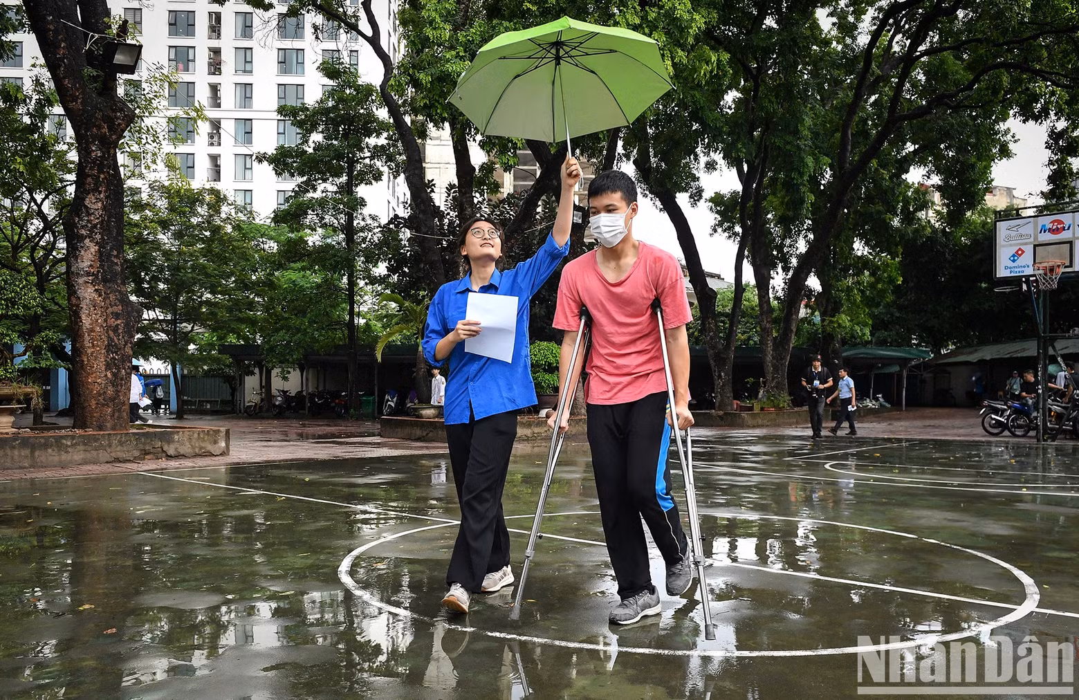 A youth volunteer holds an umbrella over Ha Duy Toan, who had to come to the exam venue on crutches because he unfortunately broke his leg right before the exam.