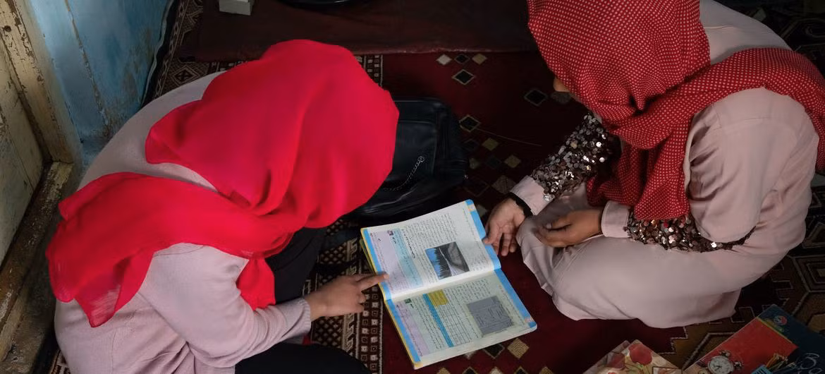 An Afghan girl studies at home with the help of her father after being denied the right to carry on studying at school. (Photo: UNICEF)