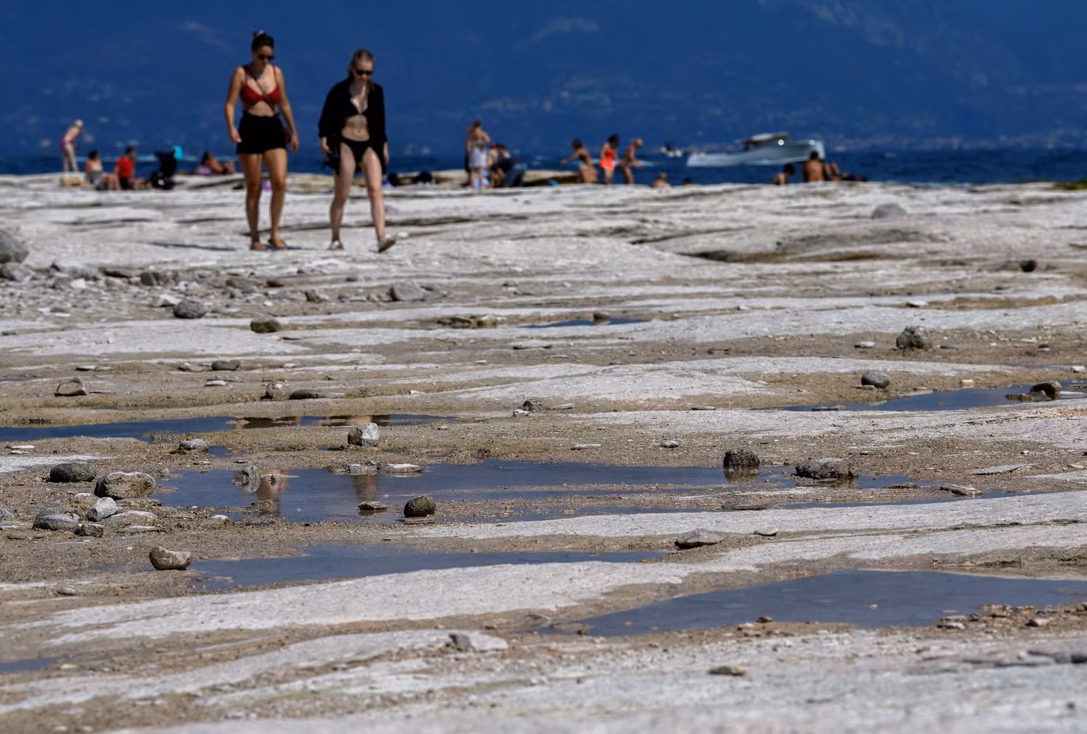 People walk as underwater rocks emerge from the water of Lake Garda after northern Italy experienced the worst drought in 70 years in Sirmione, Italy, August 16, 2022. (Photo: Reuters)