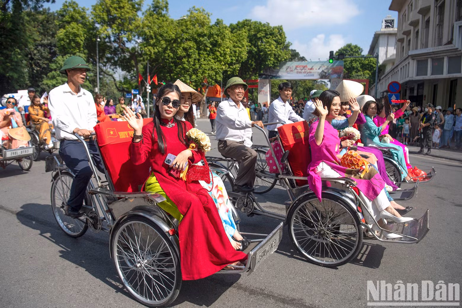 An Ao dai parade with flower-decorated cyclos moves along the Ly Thai To Monument.