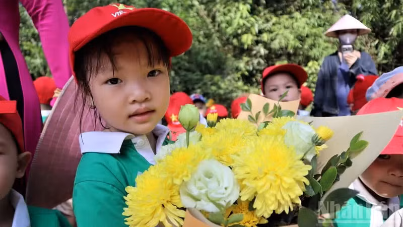 Children carrying fresh bouquets of flowers offer them to beloved Uncle Ho.