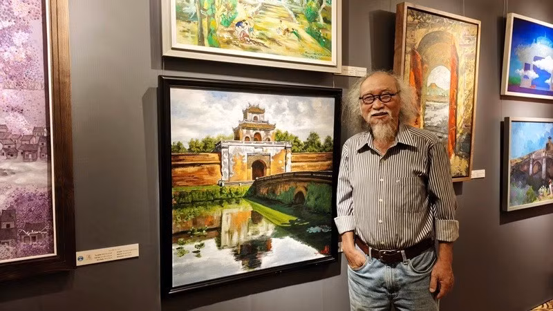 Painter Dang Mau Tuu stands beside his painting on display at the exhibition