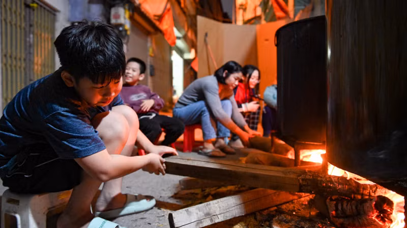 Adults and children gather and stay up all night in many alleys in Hanoi to watch over the pot of banh chung for Tet.