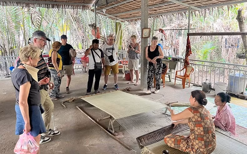 Foreign tourists watch the mat weaving process in Nhon Thanh Commune (Ben Tre City, Ben Tre Province).