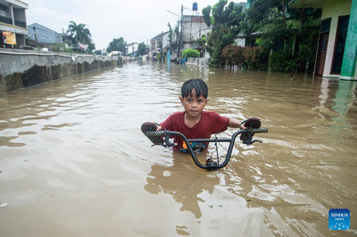 A boy pushes his bike through floodwaters in South Tangerang, Banten Province, Indonesia, Jan. 23, 2026. (Photo: Xinhua)