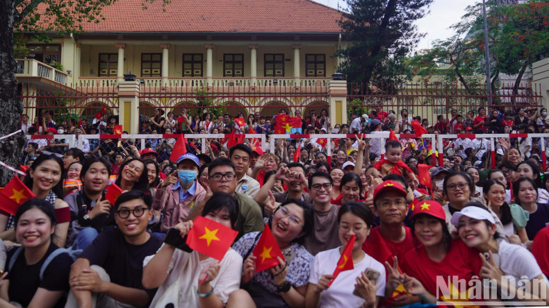 Children, accompanied by their parents, wave national flags and give smiles as they waite for the parade to approach.
