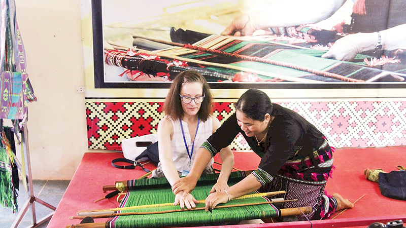 Artisan H’Binh introduces Ma brocade weaving techniques to foreign visitors at the cooperative. (Photo: nhandan.vn)