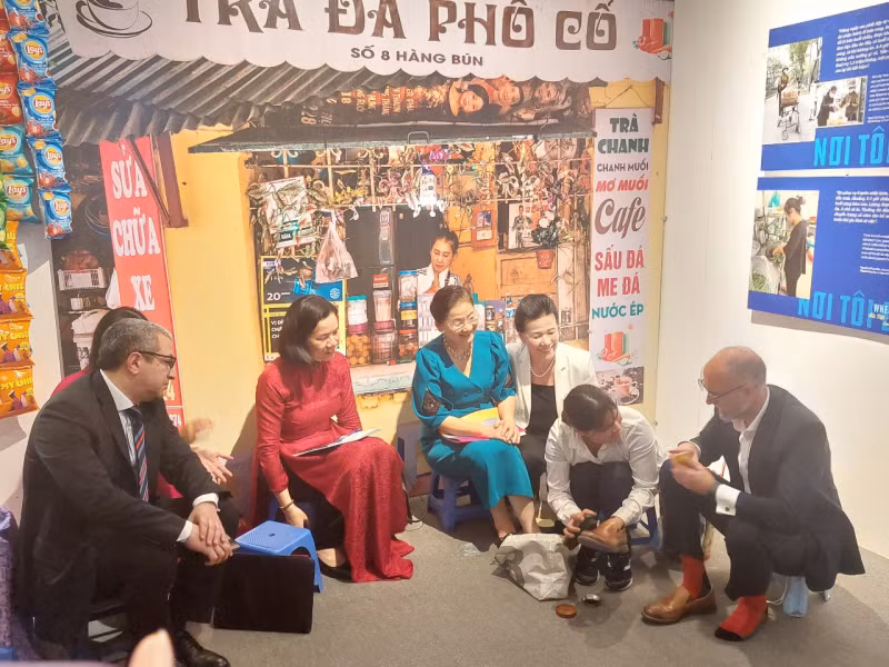 Canadian Ambassador to Vietnam Shawn Steil (first from right) gets his shoes polished by a migrant woman at the exhibition (Photo: daibieunhandan.vn)