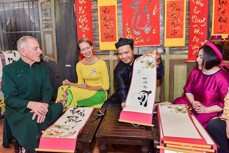 Foreigners in Vietnamese traditional long dress explore Vietnamese calligraphy (Photo: VNA)