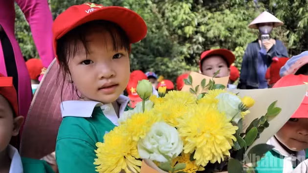 Children carrying fresh bouquets of flowers offer them to beloved Uncle Ho.