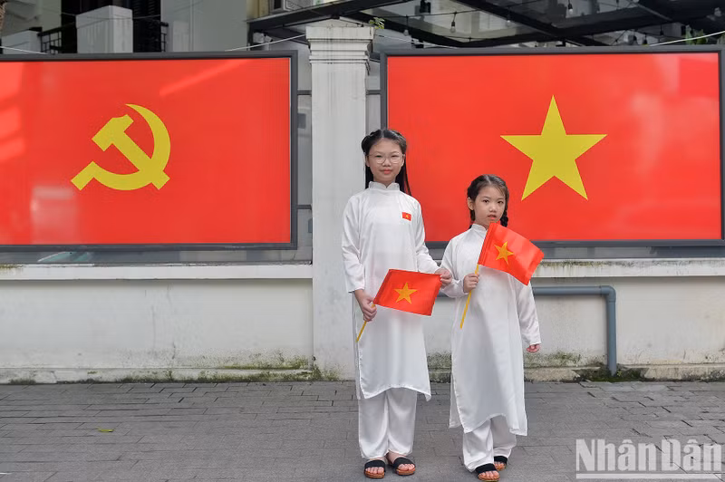 Two little girls pose for a photo with the Party flag and national flag in the background.