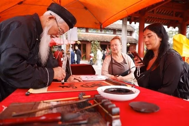 Two international tourists watch a calligrapher writing in Hanoi. (Photo: VNA)