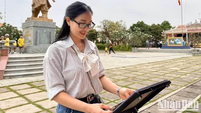 Teacher Tran Thi Bich Phuong checks in at the NFC chip-enabled board of the "Love Vietnam So Much" project by Nhan Dan Newspaper at the Nguyen Huu Canh Temple Relic Site.