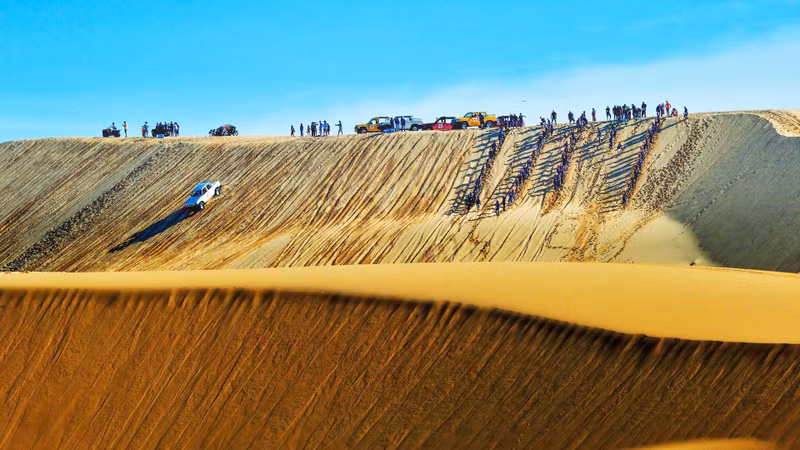 Tourists tackle dunes on off-road vehicles.